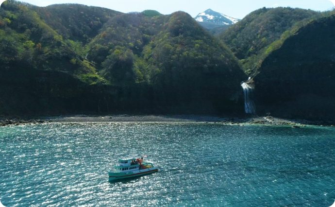 山あいの滝に近づく小型観光船おーろら